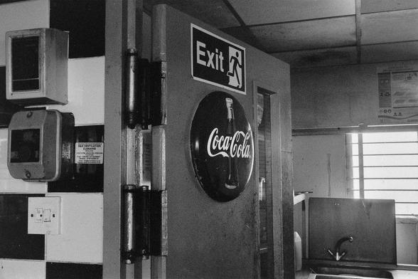 black and white photo in an old diner. door to kitchen is open, on the door is a Coca cola sign