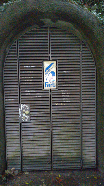 Nahaufnahme des mit einer Gittertür verschlossenen Tunneleingangss. In der Mitte des Tor ist eine weisse Hochkant-Plakette mit einem älteren Logo der FART, bestehend aus einem stilisierten Triebzug auf einer grossen Bogenbrücke.