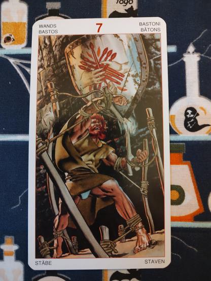 Card from the Initiatory Tarot of the Golden Dawn deck published by Lo Scarabeo.
Seven of Wands. 
A man, a redhead, wearing a simple brown tunic, is bound by various stakes and posts, but is fighting to break free.
