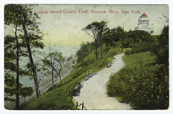 This postcard depicts a serene landscape with winding paths leading through lush greenery on an elevated terrain overlooking New York's Riverside Drive and Grant's Tomb in the distance. The foreground shows well-maintained pathways bordered by vibrant bushes and trees, suggesting it was taken during late spring or summer. A few individuals are seated along the path, enjoying the view. Architectural features include a classical building with columns at the top of the hill on the right side, indicative of a memorial structure like Grant's Tomb itself. The sky is clear blue, adding to the tranquil ambiance of this historical and cultural setting in New York City.