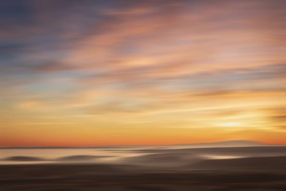 Landscape photography of evening Sunset with everything a little bit defocusing by a movement effect. You can see orange colors in the sky with some clouds.