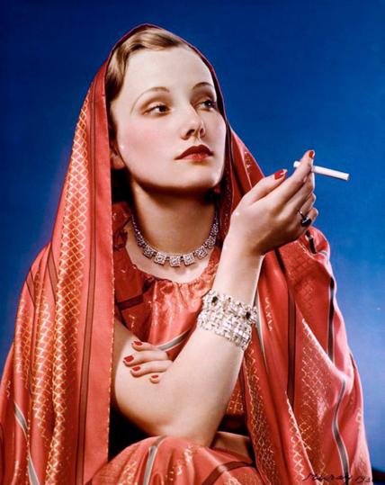 "Girl in Red" advertisement for Lucky Strike; shot by Nickolas Muray, a photographer enlisted by Bernays to help popularize feminine thinness and cigarette smoking. Show a beautiful young woman, staring off into the distance, while hold a cigarette. She is wearing lots of jewelry, an ornate red dress, and a matching red silk shawl draped over her head and shoulders. By Nickolas Muray - George Eastman House from Rochester, NY, United States via LUCKY STRIKE, GIRL IN RED"Uploaded by PDTillman, Public Domain, https://commons.wikimedia.org/w/index.php?curid=14001222
