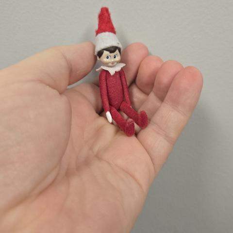 A white person's hand holding a very tiny Elf on the Shelf figure.
