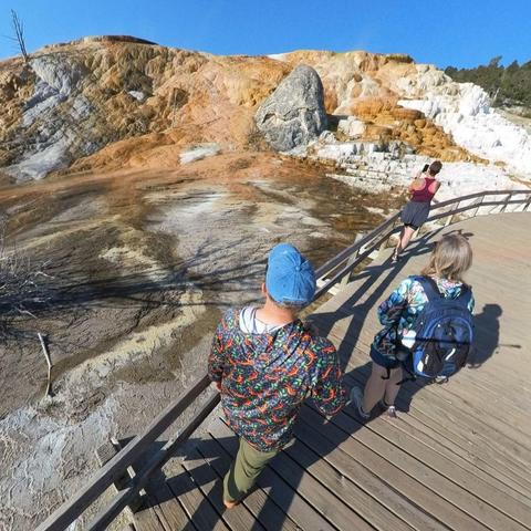 Photo of people standing on a boardwalk, observing hot springs in Yellowstone National Park.
