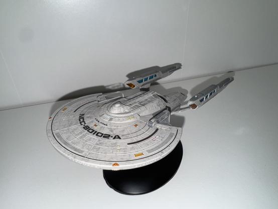 A model spaceship resembling the USS Titan (NCC-80102-A) from the Star Trek franchise, displayed on a black stand against a white background.