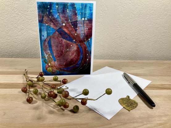 Product photo of a standing greeting card featuring an illustrated stylized version of Little Red underwater, with props and a white envelope on a wooden plank.