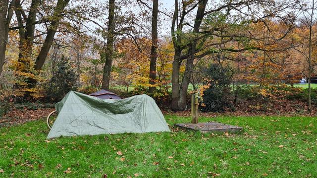 A tent that's very visibly hidden behind a dark green tarp on a field.