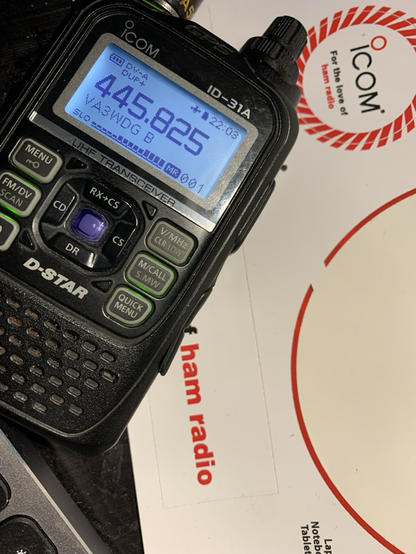 A handheld radio receiving a strong signal,sitting on a sticker sheet from icom, a major ham radio manufacturer.