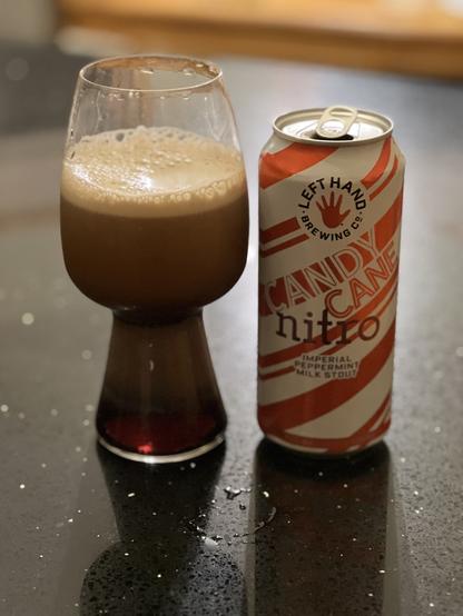 A stout glass shows nitro beer releasing its tasty bubbles. The pint can is adorned in red and white diagonal candy cane stripes, with the red LeftHand logo at the center