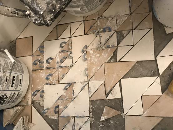 Right-isosceles triangular tiles of two colours in the process of being attached to a floor by some kind of substance.  There are upside-down U-shaped things sticking up between some pairs of tiles, presumably for keeping the spaces between them consistent.