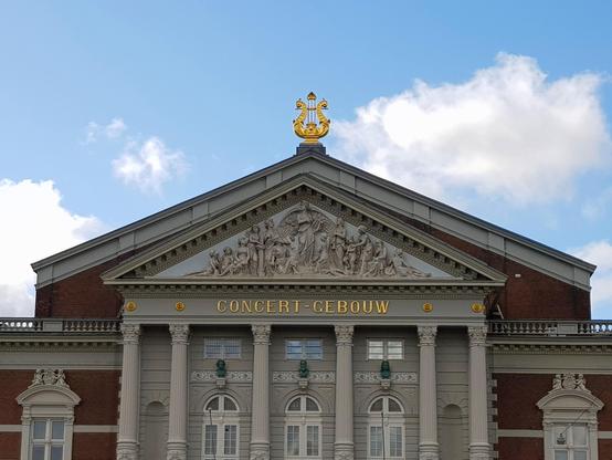 Front view of a 19th-century concert hall showing the roof topped by a golden lyra.