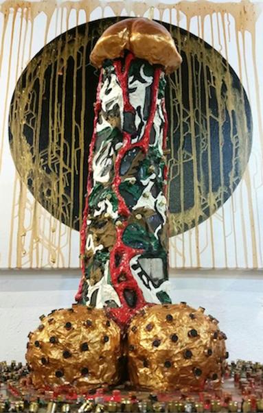 A large sculpture shaped like a phallic figure, covered with bullet casings, featuring a colorful texture with a glossy, golden top and swirls of red(representing blood) and painted in camouflage colours. The base resembles testicles, crafted in a metallic gold finish with dark accents. The background includes a circular black shape with dripping gold elements, creating a striking contrast.