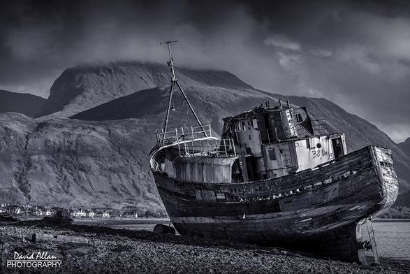 A boat lies wrecked on the shores of Loch Linnhe in the Scottish Highlands near Fort William with the brooding Ben Nevis mountain as a backdrop.