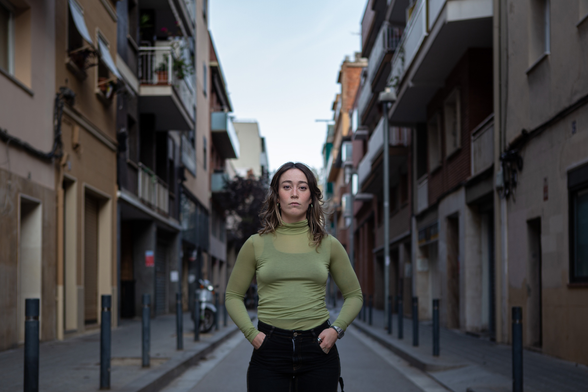 Retrat frontal de Marta Espriu, al mig d'un carrer estret. Mans a les butxaques, mirada que diria intensa i dura. Autora: Júlia Molins