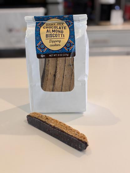 A bag of Trader Joe’s chocolate almond biscotti with one piece laying in front of the bag