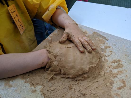 Ein Kind arbeitet mit Ton. Eine Hand ist unter dem Ton versteckt.