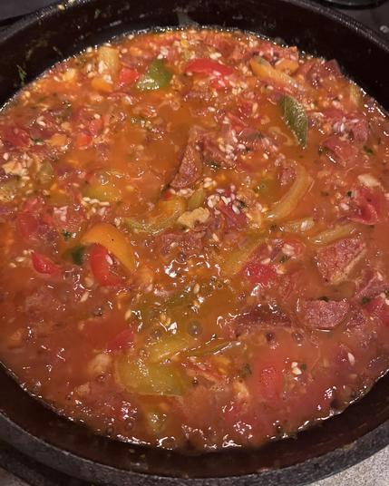 A frying pan full of paella ingredients, looking very red as the rice is not cooked