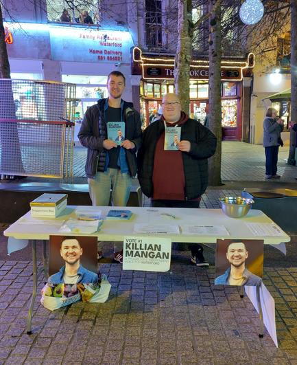 A photo of Killian and Adam behind a table covered with Killian's general election campaign material.