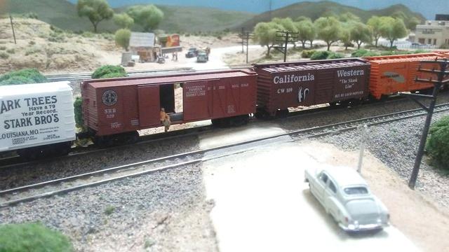 Someone is hanging off the edge of this N-scale boxcar as it goes through a railroad crossing.