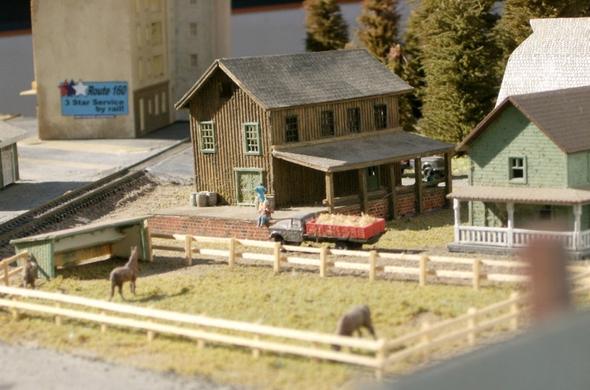 An N-scale truck full of hay is pulling up to a small house.