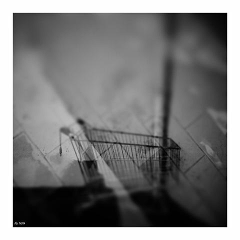 Experimentelles Schwarzweißfoto - Doppelbelichtung. Auszumachen ist ein Einkaufswagen, durch den ein gefliester Boden verläuft. Ebenfalls zu erkennen ist ein vertikales Rohr rechts von der Bildmitte. Aufgenommen mit einem Sony Xperia Z5 und Vignette for Android.