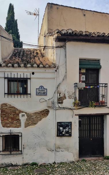 Fachada en la placeta de Capellanes. En el balcón hay decoraciones estilo budista y plantas. En algunas partes de la fachada hay huecos que dejan ver los ladrillos. Hay dos ventanas con rejas de hierro.
