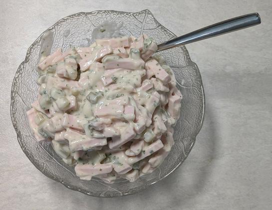 Win Glasschälchen mit Fleischsalat und einem Löffel drin.
Der Fleisch-Salat enthält fein geschnittene Wurst, kleine Gurkenwürfel, Mayonnaise und Kräuter.