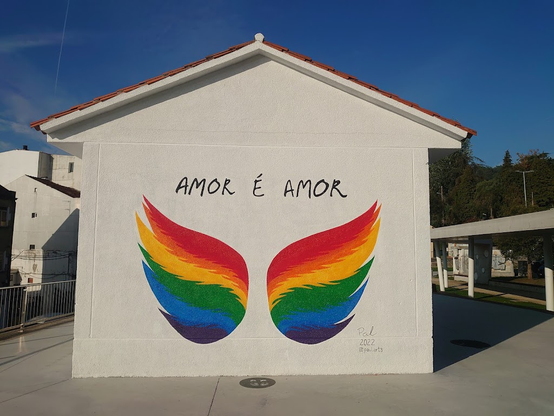 Mural orixinal da antiga estación de tren de Chapela que mostraba dúas ás coas cores da bandeira LGBTQ e o lema "amor é amor".