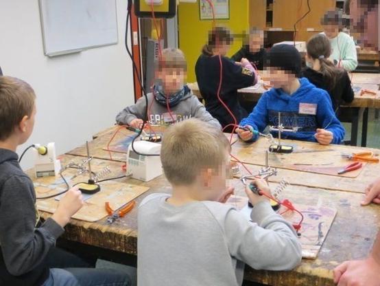 Kinder sitzen an Werktischen und löten.