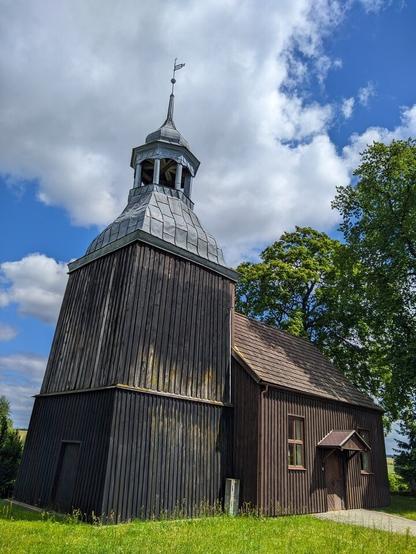 Niewielki drewniany kościół z blaszanym dachem na wieży. Z tyłu po prawej stronie widać drzewa.