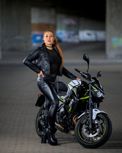 red haired girl in biking leather clothes next to a motorcycle.