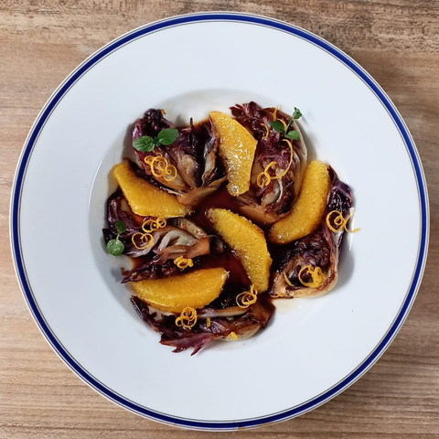 5 Spalten Radicchio + 5 Orangenfilets mit Orangenzesten garniert und etwas Sauce auf einem Teller