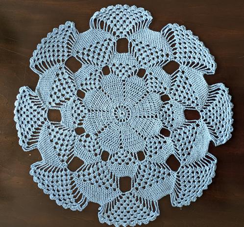 Light blue doilie 41 cm (16") across, done in a pattern that creates a 3D illusion of curving triangular shapes pointing towards a central flower pattern.