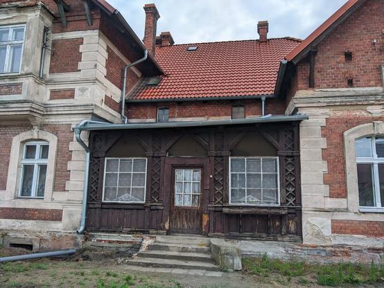 Zdobiony drewniany łącznik-wypełnienie między dwoma wystającymi częściami starego budynku zz czerwonej cegły o otynkowanych rogach.