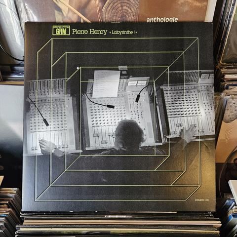 Album cover features a black and white photograph of Pierre Henry sitting before three separate mixing boards, his arms outstretched to move the levers on the left and right.