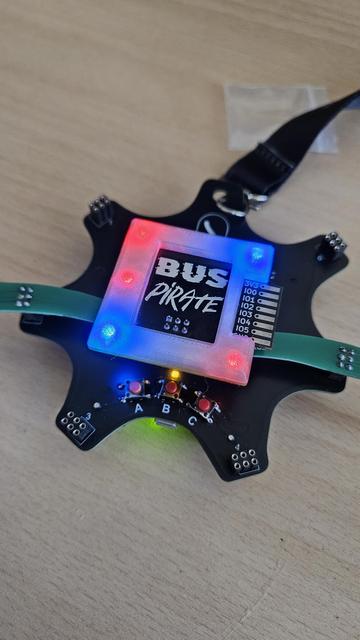 Square Bus Pirate add-on PCB, glowing, connected to the Supercon 8 badge.