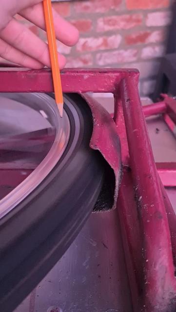 A close-up of a fast spinning bicycle tire. It's surrounded by chrome and a red pink frame. A hand is moving a pencil tip close to the rim.