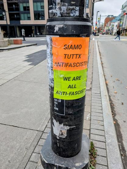 Orange and Green paper signs are taped to a pole on Spring Garden Road in Halifax. One of the signs reads "we are all anti-fascist".