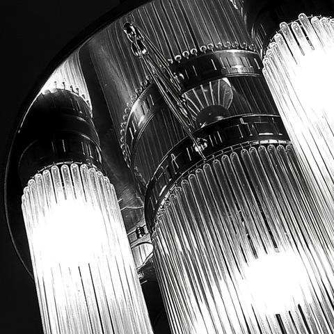 A chandelier with many thin long glass tubes that are bundled in several cylindrical shapes and reflected on a brass plate to which they are attached