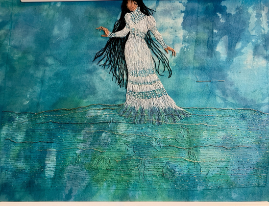 An embroidered panel of glittering water with faces and hands submerged in it, with La Llorona wading in a long white gown, long black hair flying around her.
