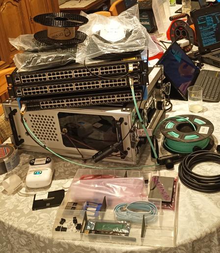 Auf einem tisch liegt ein 19 zoll computer auf dem sich 3 switche stapeln. Davor liegen Netzwerkkarten daneben spulen mit Glasfaser kabeln.