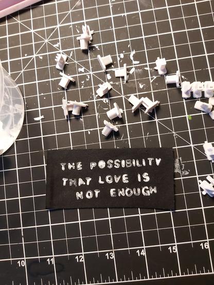 a black patch with white stamped font, with little letter stamps scattered around. the patch reads: "the possibility that love is not enough"