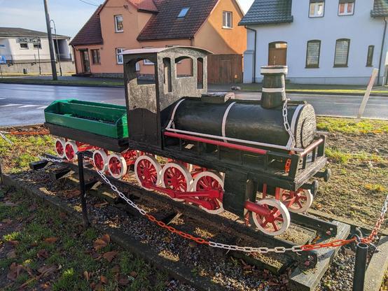 Drewniana miniatura czarnej lokomotywy parowej z zielonym wagonem.