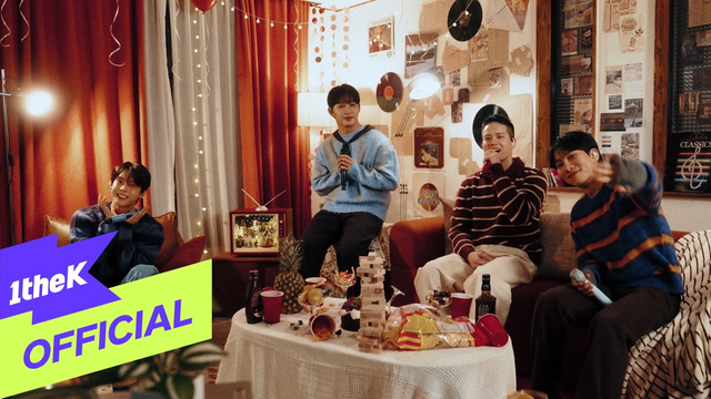 BTOB Be Alright Live Clip Screenshot. They're in a living room, with balloons and streamers and remnants of a party on the coffee table. The band members are wearing cute fluffy sweaters. The vibe is chill.