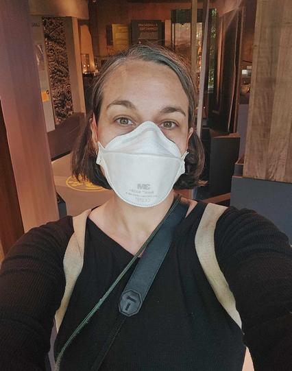 A colour photograph of a woman wearing a white ffp3 mask and looking at the camera.