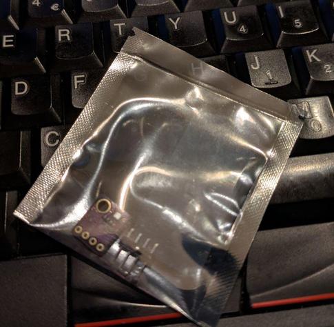 Silver coloured plastic antistatic bag resting on a ThinkPad keyboard. There's a thermal seal line near the top and two tear point notches on the outside of the seal, making them useless.