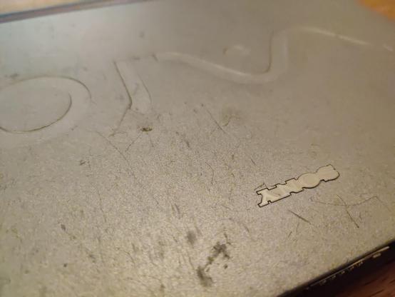 A close-up of the badly scuffed lid of the machine. The silvery-grey eggshell finish is densely packed with short scratches and scuffs.