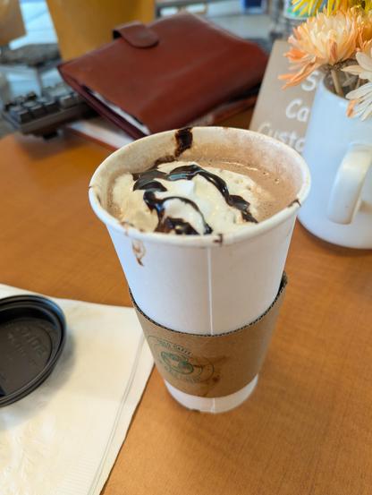 Disposable coffee cup full of hot chocolate with whipped cream and chocolate drizzle on top 

There was more whipped cream before the picture but I slurped it off