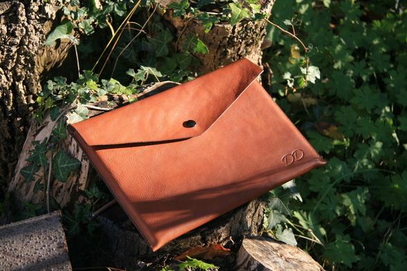 Housse de tablette en cuir clair, fermée, dans un décor naturel.