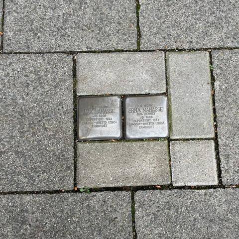 Zwei Stolpersteine in Mönchengladbach. Sie sind grau angelaufen und haben dadurch die gleiche Farbe wie die umgebenden Wegplatten.